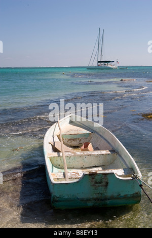 Un petit bateau est lié à un jeu dans les bas-fonds avec des voiliers à l'horizon sous un soleil d'après-midi chaud : Ambergris Caye, Belize Banque D'Images