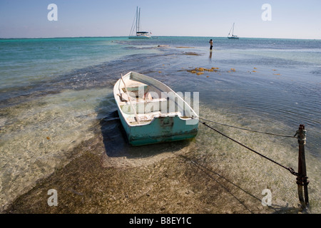 Un petit bateau est lié à un jeu dans les bas-fonds avec des voiliers à l'horizon sous un soleil d'après-midi chaud : Ambergris Caye, Belize Banque D'Images