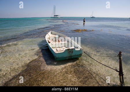 Un petit bateau est lié à un jeu dans les bas-fonds avec des voiliers à l'horizon sous un soleil d'après-midi chaud : Ambergris Caye, Belize Banque D'Images