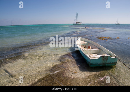 Un petit bateau est lié à un jeu dans les bas-fonds avec des voiliers à l'horizon sous un soleil d'après-midi chaud : Ambergris Caye, Belize Banque D'Images