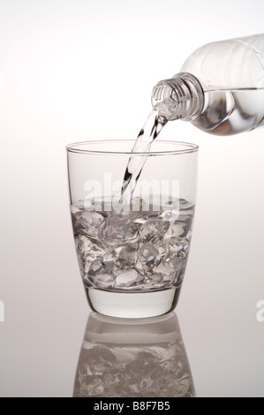 On verse de l'eau d'une bouteille d'eau dans un verre rempli de glaçons Banque D'Images