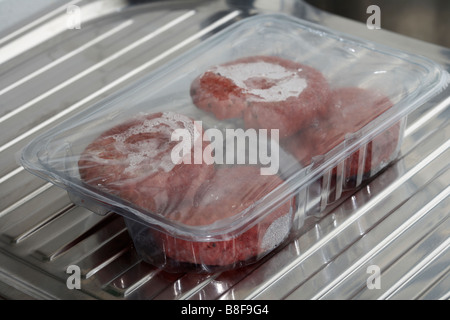 Quatre beefburgers dans un bac en plastique la décongélation à température ambiante sur une surface drainante d'évier de cuisine Banque D'Images