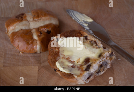 Hot cross bun grillé unique assise sur un billot en bois recouvert de propagation à l'aide d'un couteau Banque D'Images