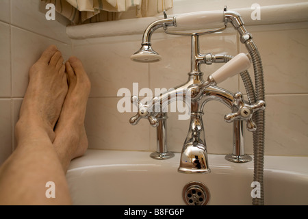 Deux pieds sur le bord de la baignoire dans la salle de bains robinetterie montrant Banque D'Images