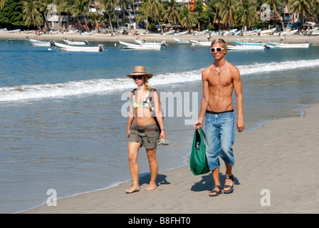 Or bronzé-haired young couple promenade sur la plage au bord de l'Harbour Harbour à Puerto Escondido. Oaxaca, Mexique Banque D'Images