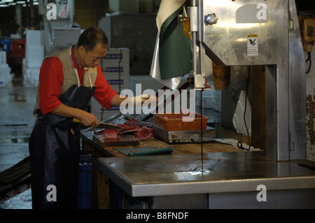 Un travailleur se prépare à vendre du poisson au marché aux poissons de Tsukiji à Tokyo. En face est une scie à ruban utilisé pour couper le thon congelé Banque D'Images