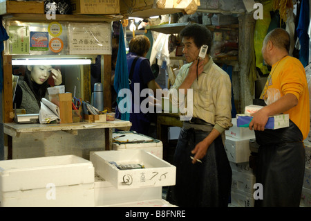 Un commerçant à la Tokyo Tsukiji fish market parle sur son téléphone mobile. Un caissier travaille dans son stand. Banque D'Images
