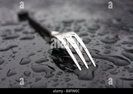 Une fourchette à dîner sur une surface métallique lisse avec des gouttes de pluie Banque D'Images