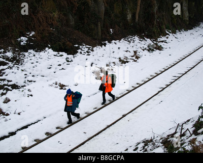 Deux hommes en vestes haute visibilité orange marche sur une ligne de chemin de fer en milieu rural dans la neige Banque D'Images