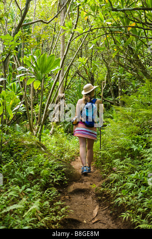 Femme marche avec un personnel à pied à travers une forêt tropicale sur la côte de Na Pali de Kauai Hawaii Banque D'Images