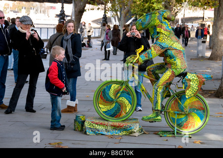 Un garçon regardant un spectacle de rue et aux touristes de prendre des photographies, sur une bicyclette, Caméléon Banque D'Images