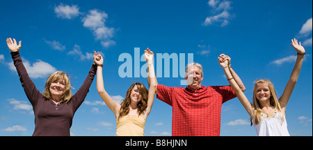 Belle famille tenant la main et levant les bras contre un ciel bleu Banque D'Images