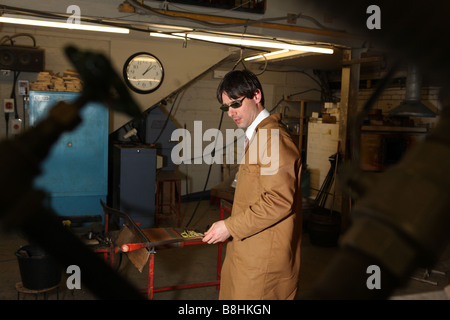 Un souffleur de verre professionnel prend du verre en fusion sur une chaudière prête à exploser et la forme dans un vase ou verre ornement Banque D'Images