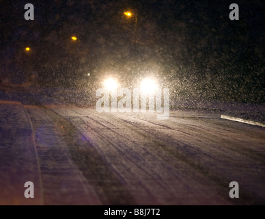 Les phares d'une voiture la nuit car il entraîne à travers une tempête de neige à Redditch, Worcestershire, Royaume-Uni Banque D'Images
