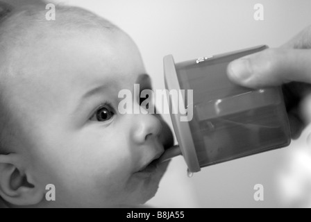 Un petit garçon boit de l'eau d'un bécher bébé tenu par son père. Banque D'Images