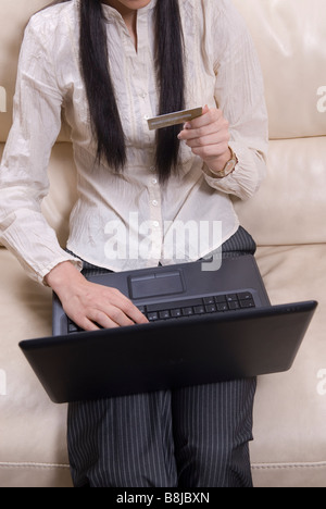 Femme était assise sur le canapé faisant des achats en ligne avec un ordinateur portable et une carte de crédit Banque D'Images