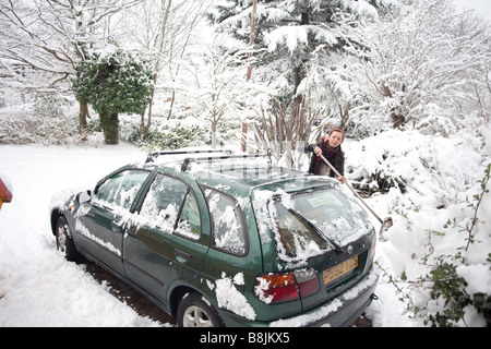 Une fille efface une voiture de la neige dans une banlieue de neige scène de rue à Thames Ditton Surrey UK Février 2009 Banque D'Images