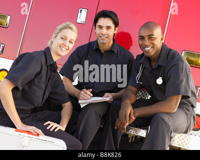 Trois ambulanciers chatter et faire de la paperasserie, assis par leur ambulance Banque D'Images