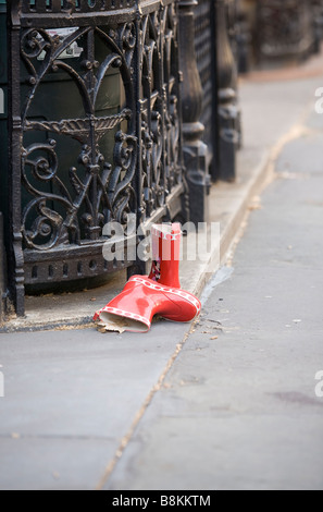 Une paire de bottes rouge pour enfants abandonnés s'asseoir sur un trottoir de la ville. Banque D'Images