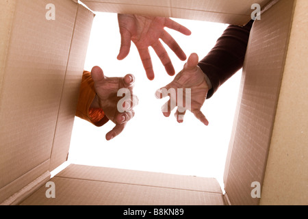 Vue de l'intérieur de boîte en carton avec trois mains en essayant d'atteindre le contenu selective focus Banque D'Images
