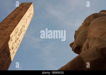 Colosse statue du pharaon Ramsès II et obélisque sculpté d'hiéroglyphes sur fond de ciel bleu, ruines du temple de Louxor, Thèbes, Egypte Banque D'Images