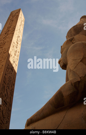 Colosse statue du pharaon Ramsès II et obélisque sculpté d'hiéroglyphes sur fond de ciel bleu, ruines du temple de Louxor, Thèbes, Egypte Banque D'Images