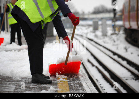 Les travailleurs d'entretien ferroviaire effacer la plate-forme couverte de neige à Wimbledon, au sud ouest de Londres. Banque D'Images