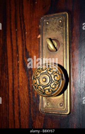 Poignée de porte en laiton décoré de meubles anciens, ca. Années 1920, montrant de blocage et d'flowery pattern design sur panneau de chêne Banque D'Images