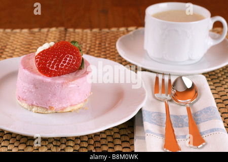 Des fraises fraîches gâteau de fantaisie avec la moitié d'un fruit sur le dessus et une tasse de cappuccino Banque D'Images