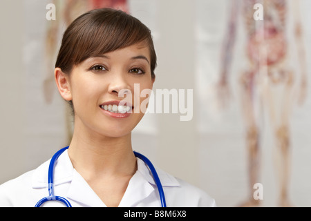 Une jolie jeune infirmière avec un stéthoscope tourné dans un hôpital avec l'anatomie humaine cartes marines hors focus derrière elle Banque D'Images