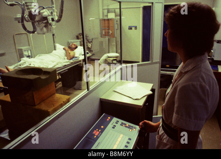 Un patient est allongé sur un lit pour un x-ray pendant que le radiologue est derrière un écran protecteur Banque D'Images