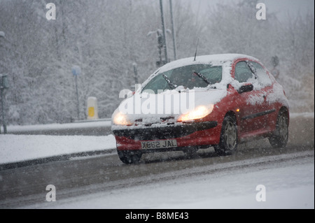 Voiture roulant lentement sur une route enneigée en hiver en Angleterre avec croisement couvertes de neige Banque D'Images