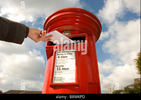 Une lettre est postée d'un rouge lumineux Royal Mail post box dans le Worcestershire en Angleterre Banque D'Images