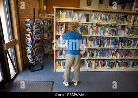 Garçon de huit ans qu'une sélection d'étagères dans une bibliothèque publique, united states Banque D'Images