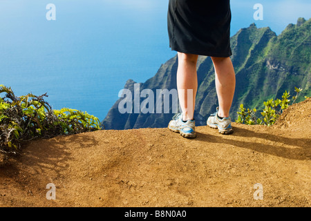 Pieds et Jambes de femme debout sur le Pihea Trail surplombant la vallée Kalalau sur la côte de Na Pali de Kauai, Hawaii, USA. Banque D'Images