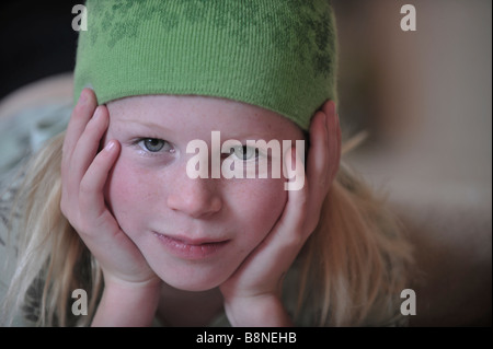 Petite fille avec sa tête dans ses mains portant un chapeau en laine vert les yeux dans la caméra Banque D'Images