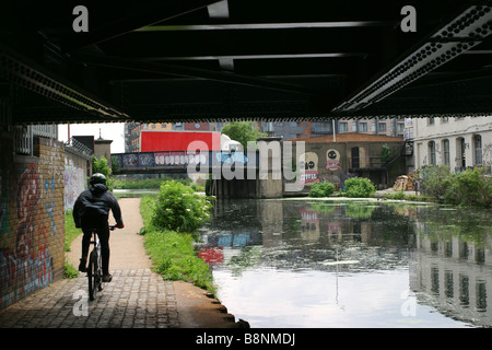 Un cycliste sur un chemin du canal au-dessous d'un pont. Banque D'Images