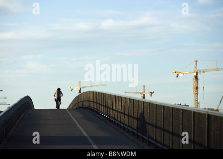 La Suède, Stockholm, bicyclist riding over bridge, des grues en arrière-plan Banque D'Images