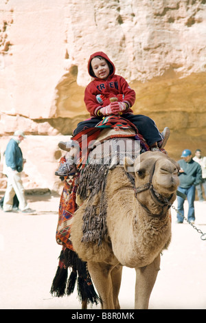 Un jeune garçon enfant tourisme bénéficiant d monté sur un chameau, Petra, Jordanie, Moyen-Orient Banque D'Images