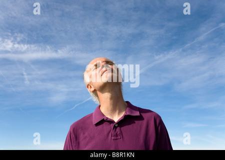Un homme d'âge moyen s'élève contre le ciel bleu, sentir la chaleur du soleil sur son visage. Banque D'Images
