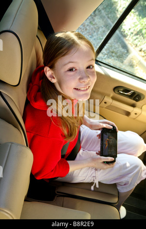 Les jeunes, heureux, smiling girl s'amuse à l'arrière d'une voiture avec un jeu électronique, psp Banque D'Images