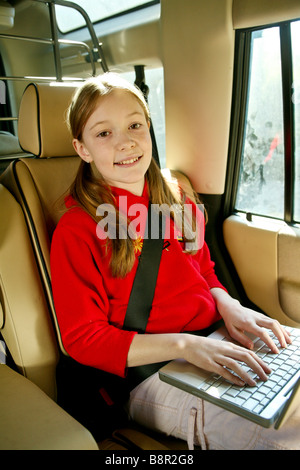 Souriant, heureux jeune fille s'amuse à l'arrière d'une voiture avec un ordinateur portable Banque D'Images