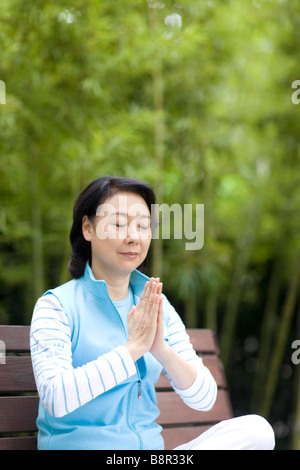 Senior woman sitting on bench en position de prière en plein air Banque D'Images