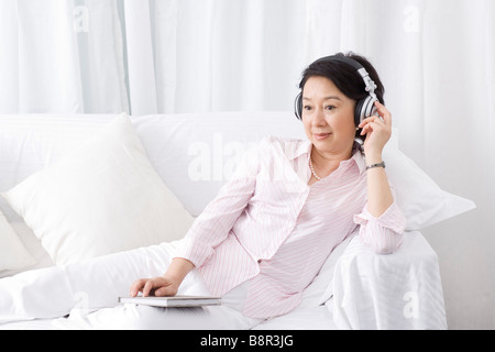 Senior woman sitting on sofa listening music avec casque Banque D'Images
