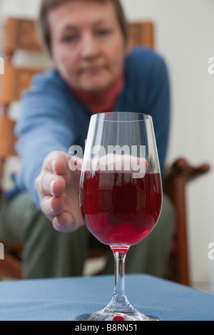 Une femme mature seule à besoin d'un verre assis à prendre un verre de vin rouge sur une table à l'avant. Angleterre Royaume-uni Grande-Bretagne Banque D'Images