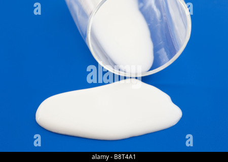 Du lait s'est renversé d'un verre sur une surface bleue. Ne pleurez pas sur le concept de phrase de capture de lait renversé. Concept de malchance Banque D'Images