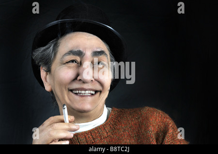 Portrait sur fond noir de maturité artistique femme souriante avec chapeau et cigarette à la main Banque D'Images