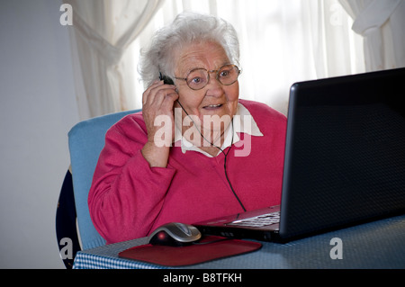 Femme âgée et ordinateur portable isolant le covid-19 et écouteurs étonnés par le zoom de chat vidéo avec des amis de famille sur son écran d'ordinateur portable Banque D'Images