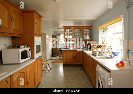 Cuisine dans la cuisine rurale de pays fatiguée dans la nécessité de rénovation avec sol de lilo et placards de cuisine dans un style des années 1980 Banque D'Images