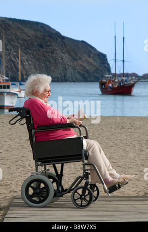 Satisfait de personnes âgées handicapées dame assise dans son fauteuil en lisant un livre dans une maison de vacances en bord de mer plage vacances Banque D'Images